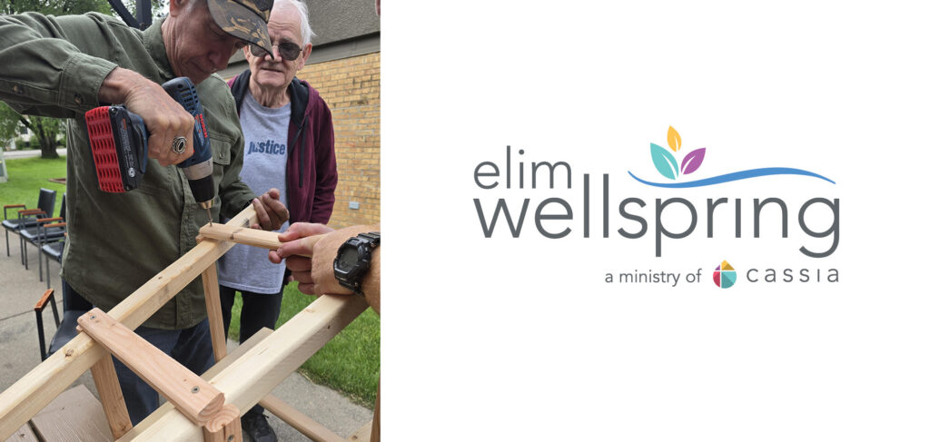 Jerry, a resident at Elim Oasis Adult Day Services, uses a power drill to work on a woodworking project, with a staff member assisting him. Another resident observes in the background, showcasing a hands-on activity that engages participants.